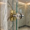 Soportes de cristal para duchas de latón y cromo sujetando un panel de ducha de cristal sin marco en un baño de mármol de estilo vintage