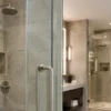 Tirador de puerta de ducha sin marco de acero inoxidable cepillado instalado en un recinto de ducha de cristal transparente en un baño de hotel contemporáneo