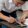 Quality inspector examining a shower hinge sample with callipers beside specification sheets