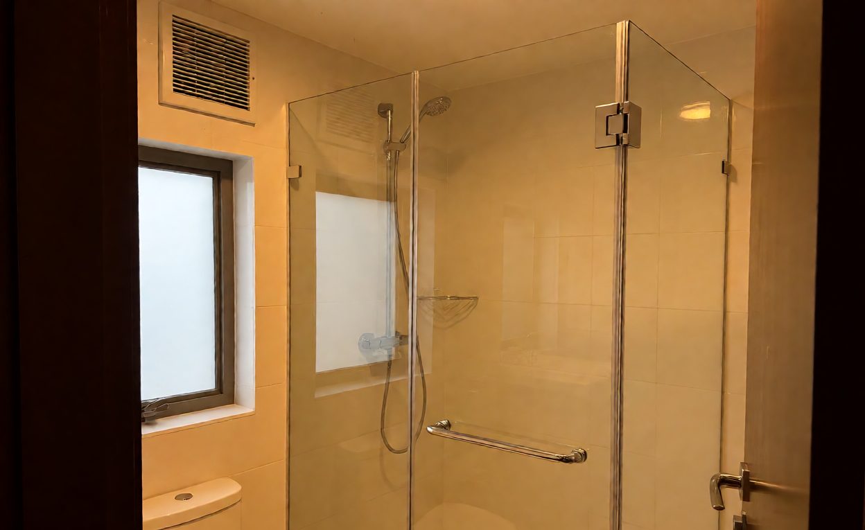 Shower Hardware In A Hotel Bathroom Environment Indoor hotel bathroom with frameless shower hardware near a window and ventilation grille
